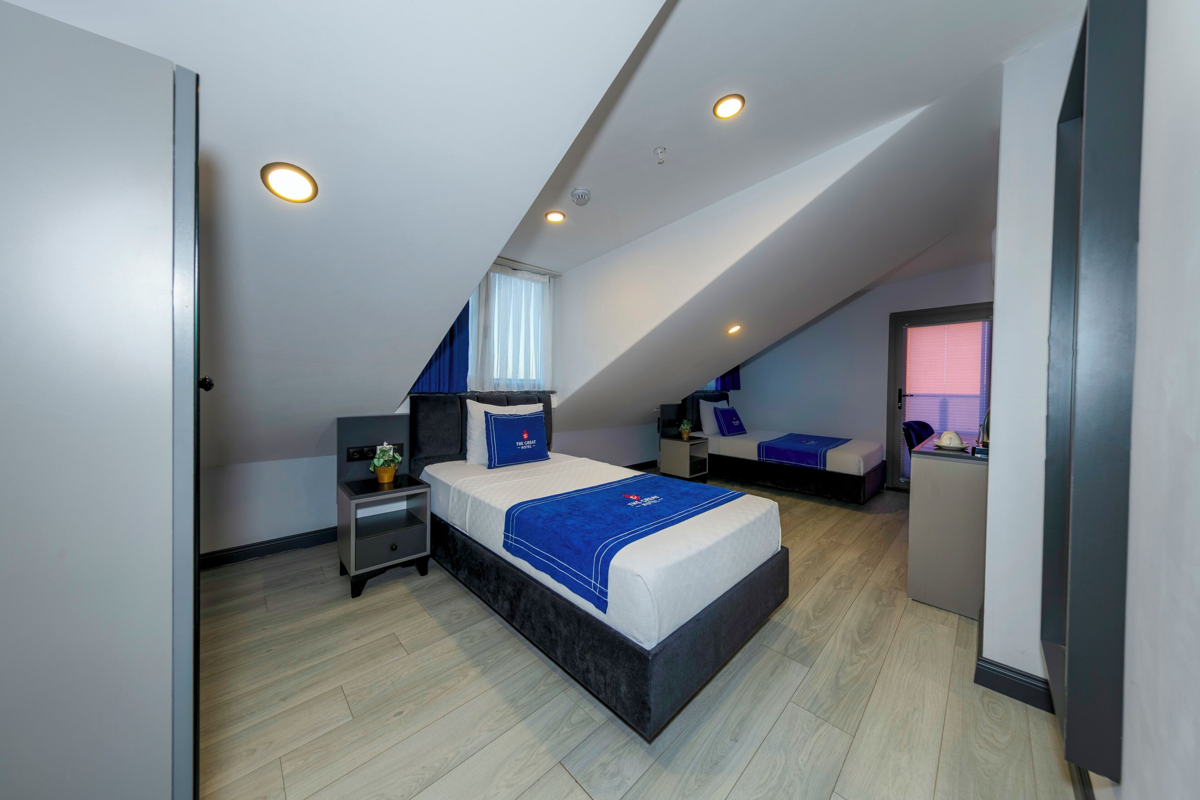 A modern bedroom with a large bed, a desk, and a chair, featuring a sloped ceiling and built-in lighting.