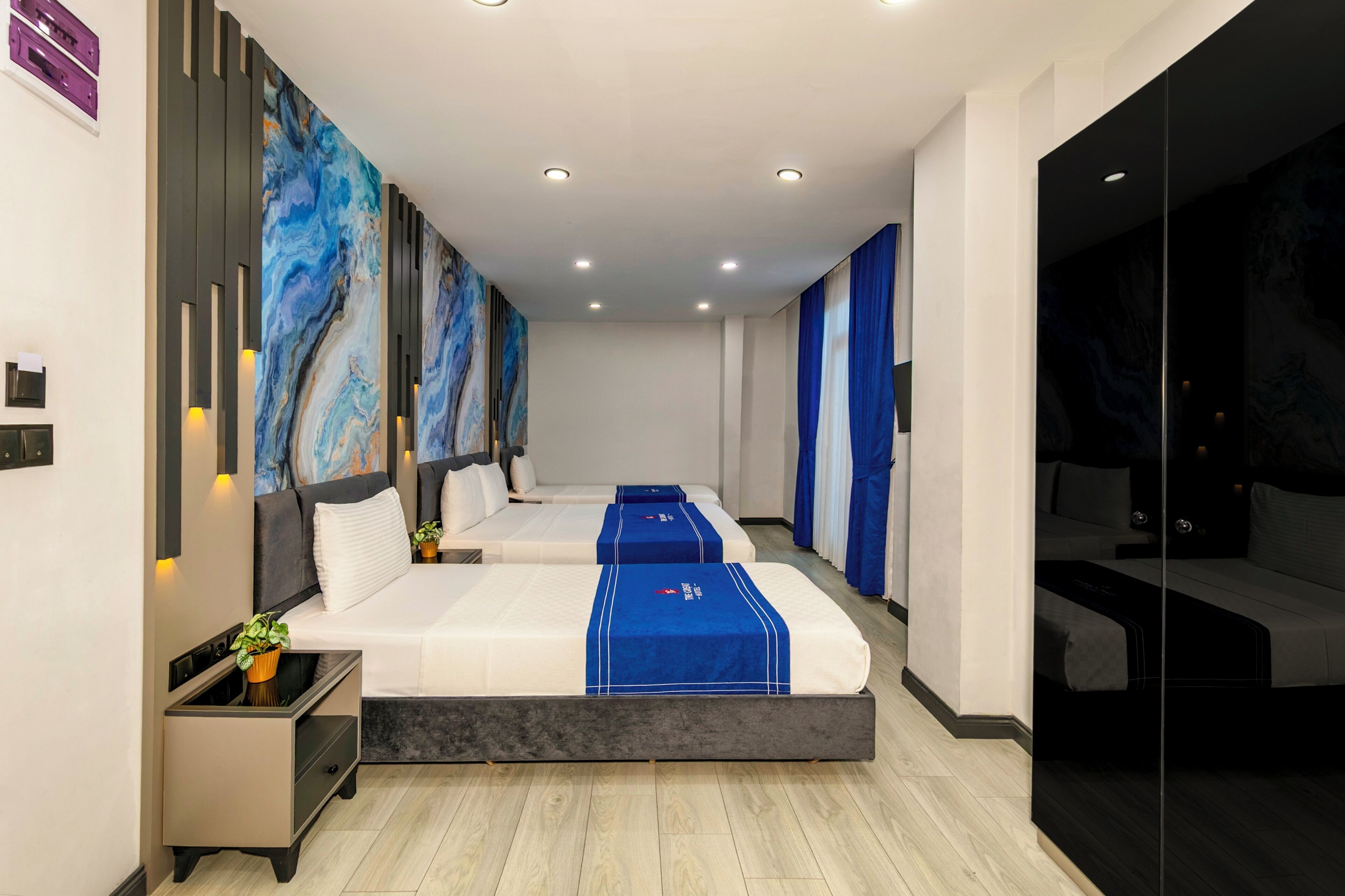 A modern hotel room with two beds, a large abstract painting on the wall, and a small bedside table with a plant.