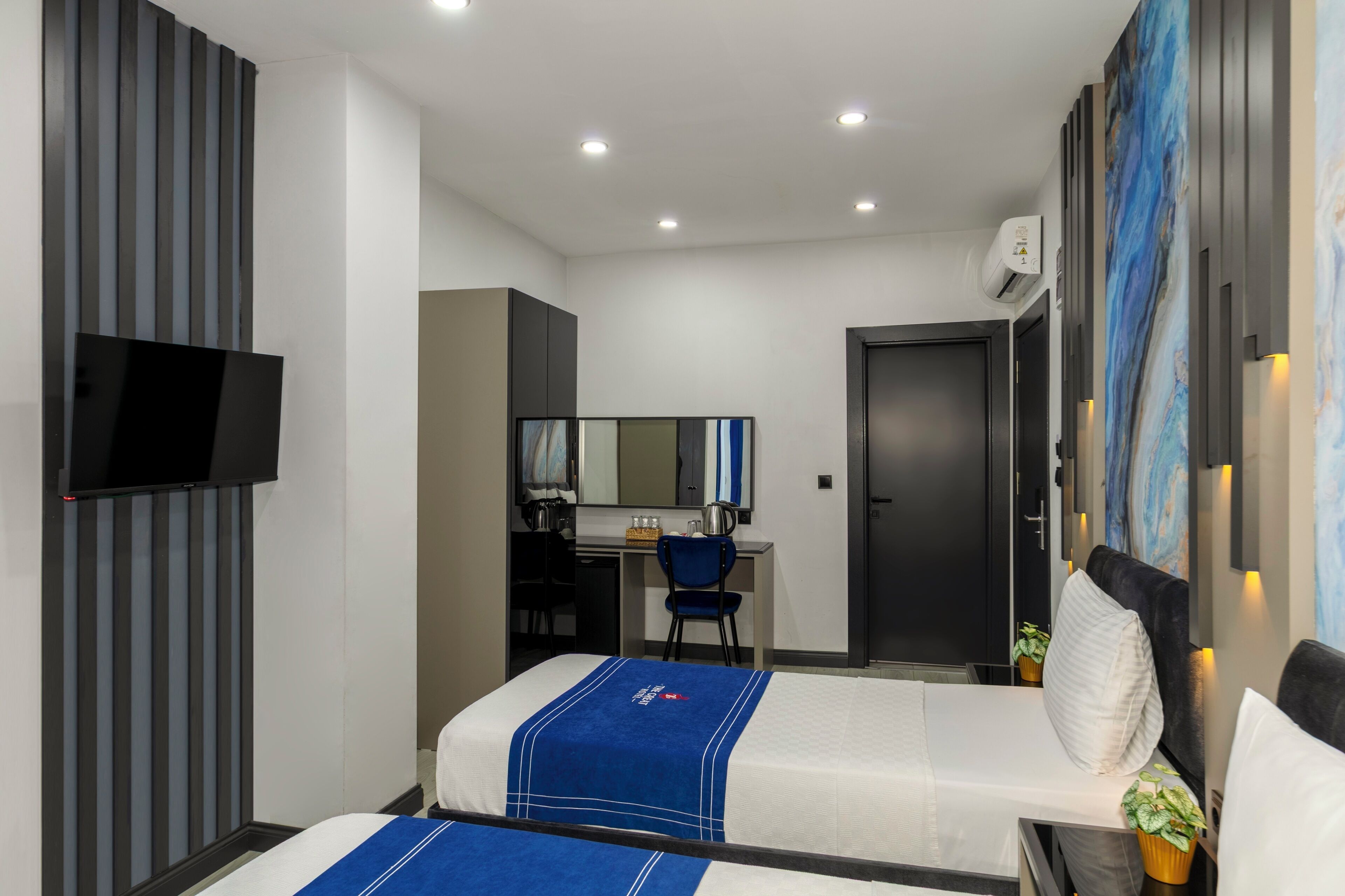 A modern hotel room with a bed, a desk, a chair, a TV, and a door.