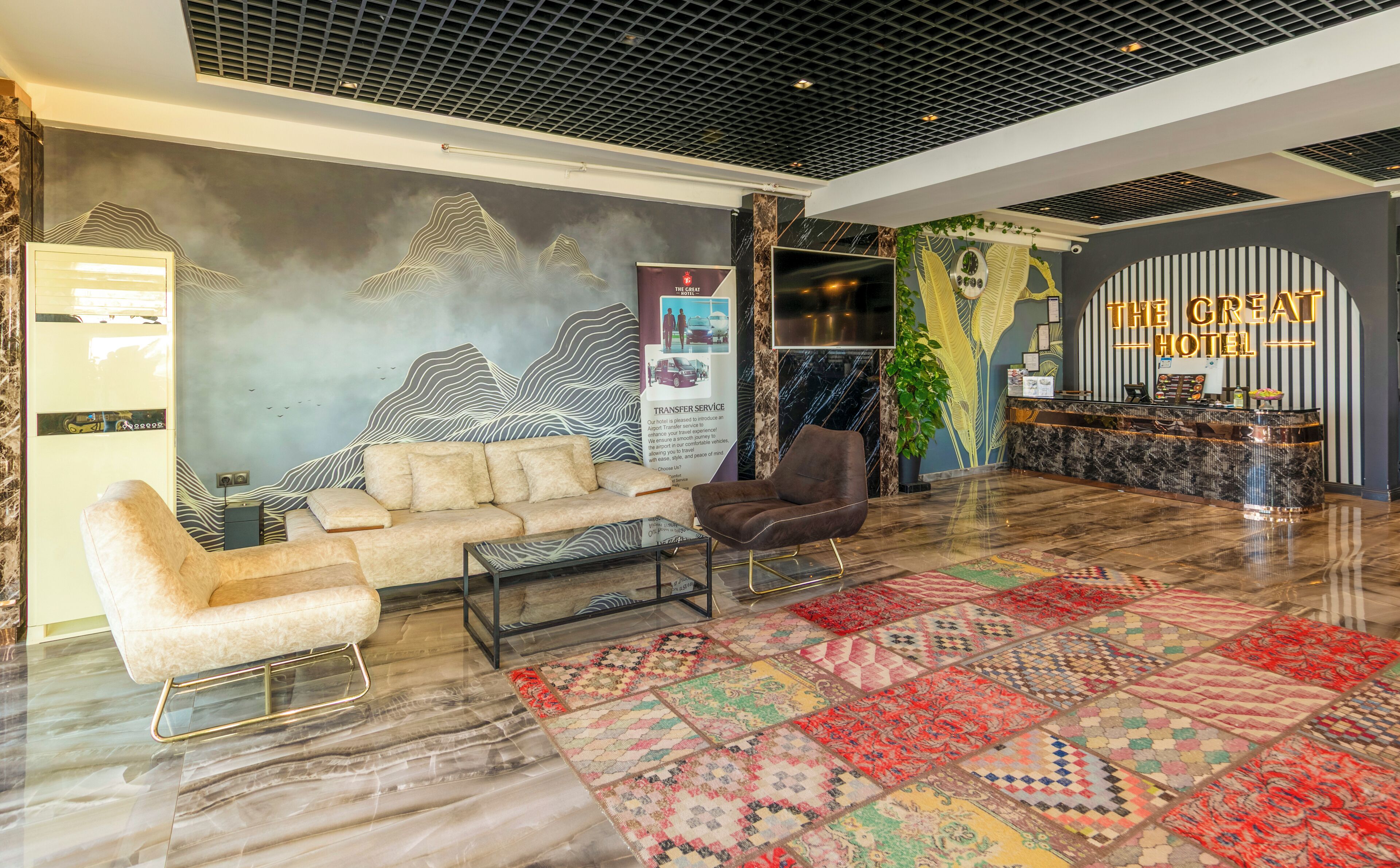 A hotel lobby with a modern design, featuring a sofa, armchairs, a patterned rug, and a reception desk.