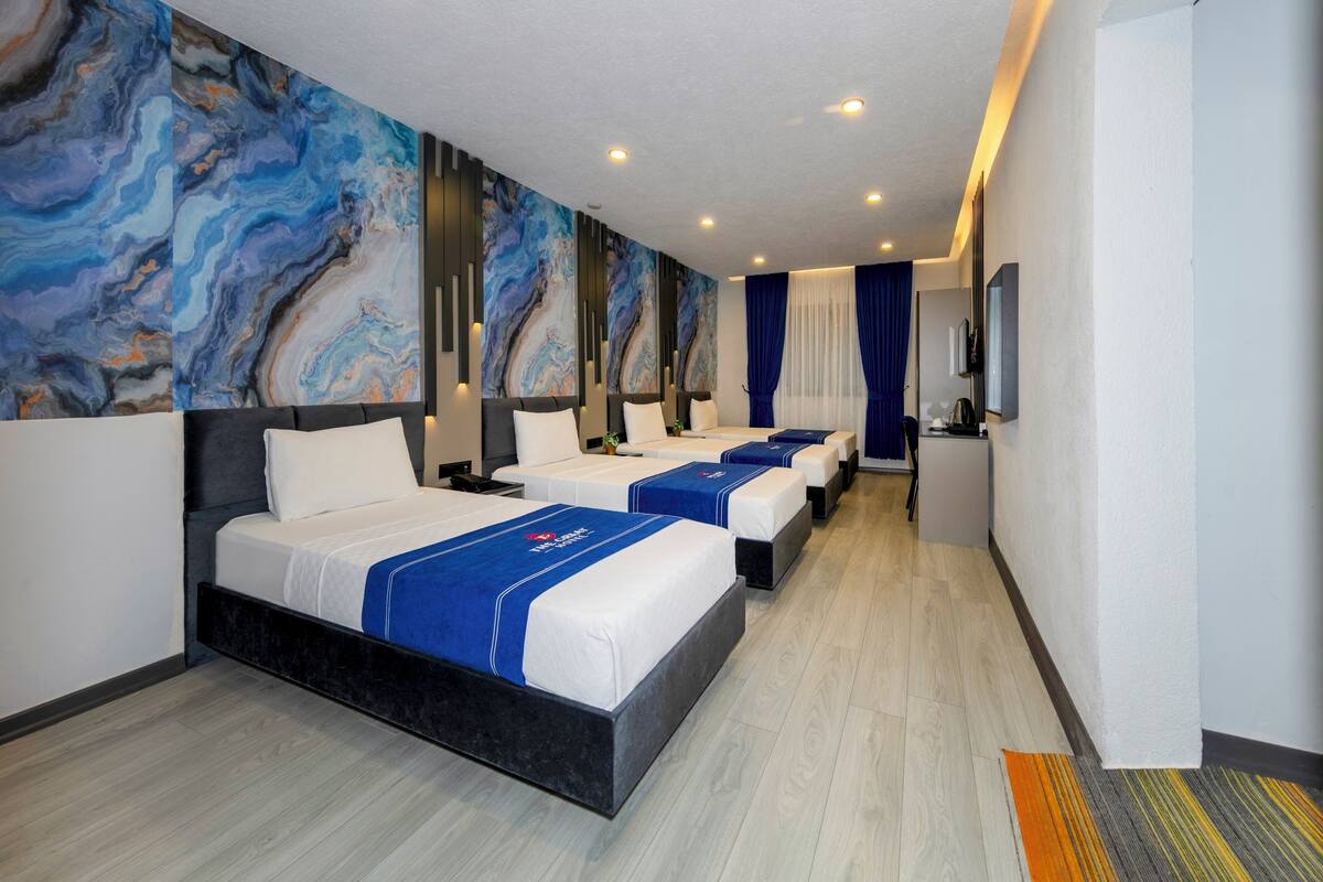 A hotel room with three beds, a large abstract mural on the wall, and a small kitchenette.