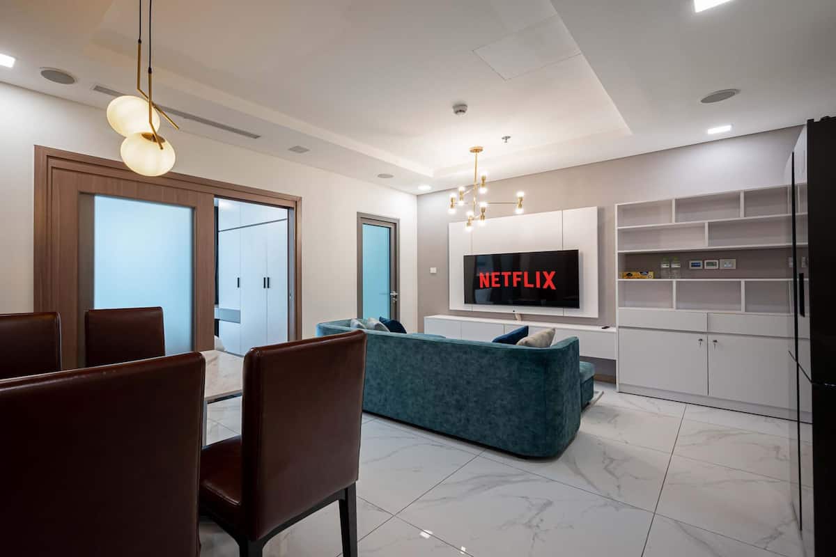 A modern living room with a dining area, a teal sofa, and a TV displaying 'NETFLIX'.