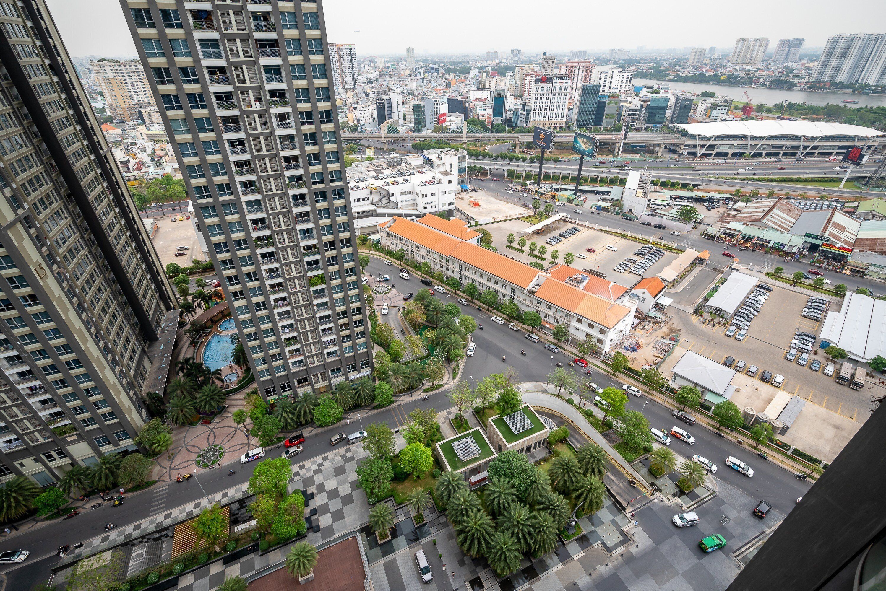 Un edificio alto con piscina en la azotea, rodeado de vegetación y una calle concurrida llena de coches y peatones.