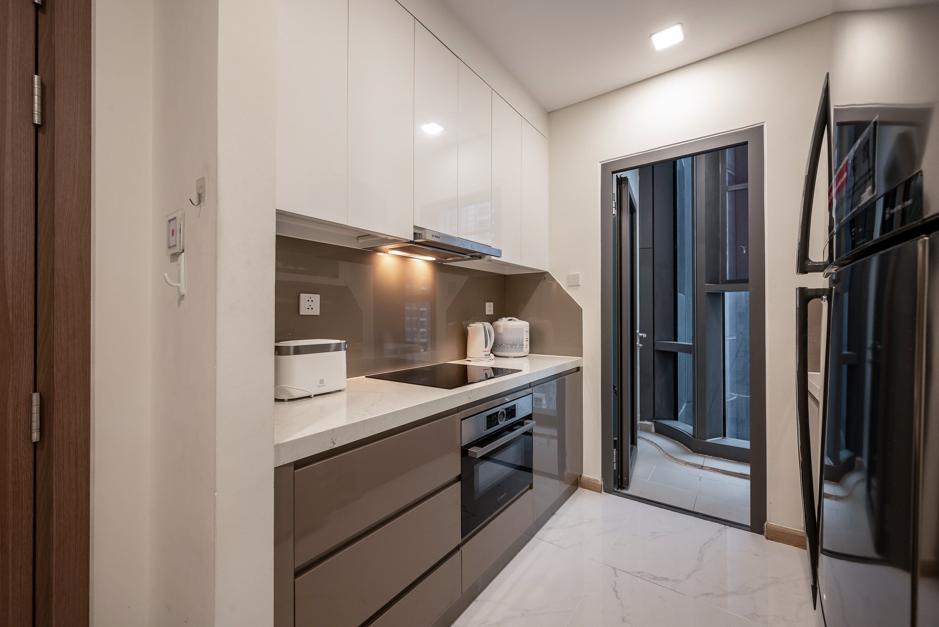 A modern kitchen with a built-in oven, a sink, and a stove. There is a window providing natural light and a door leading to another room.