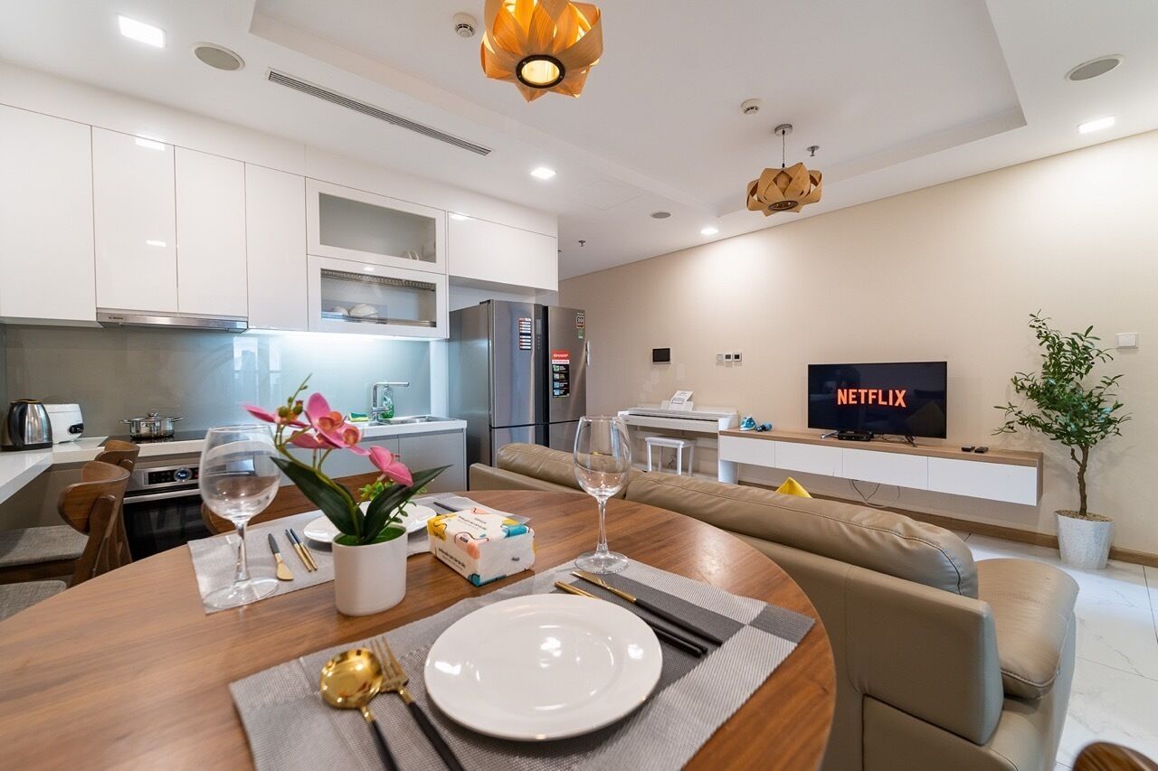 A modern living room with a dining area, a kitchen, and a TV displaying 'NETFLIX'.