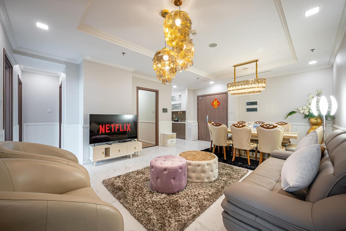 A modern living room with a TV, sofas, ottomans, and a chandelier.