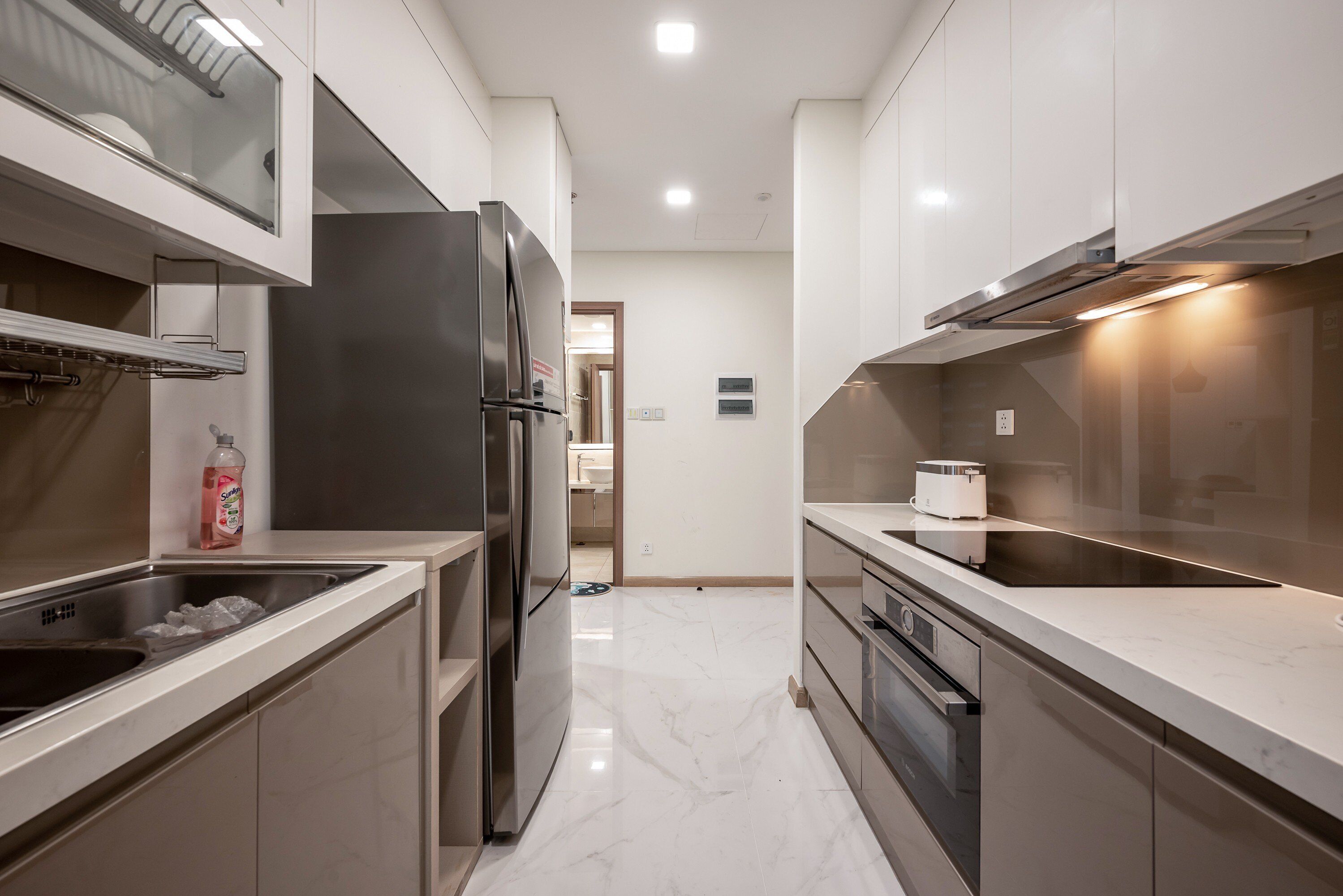 A modern kitchen with stainless steel appliances, a marble countertop, and a view into the adjacent bathroom.