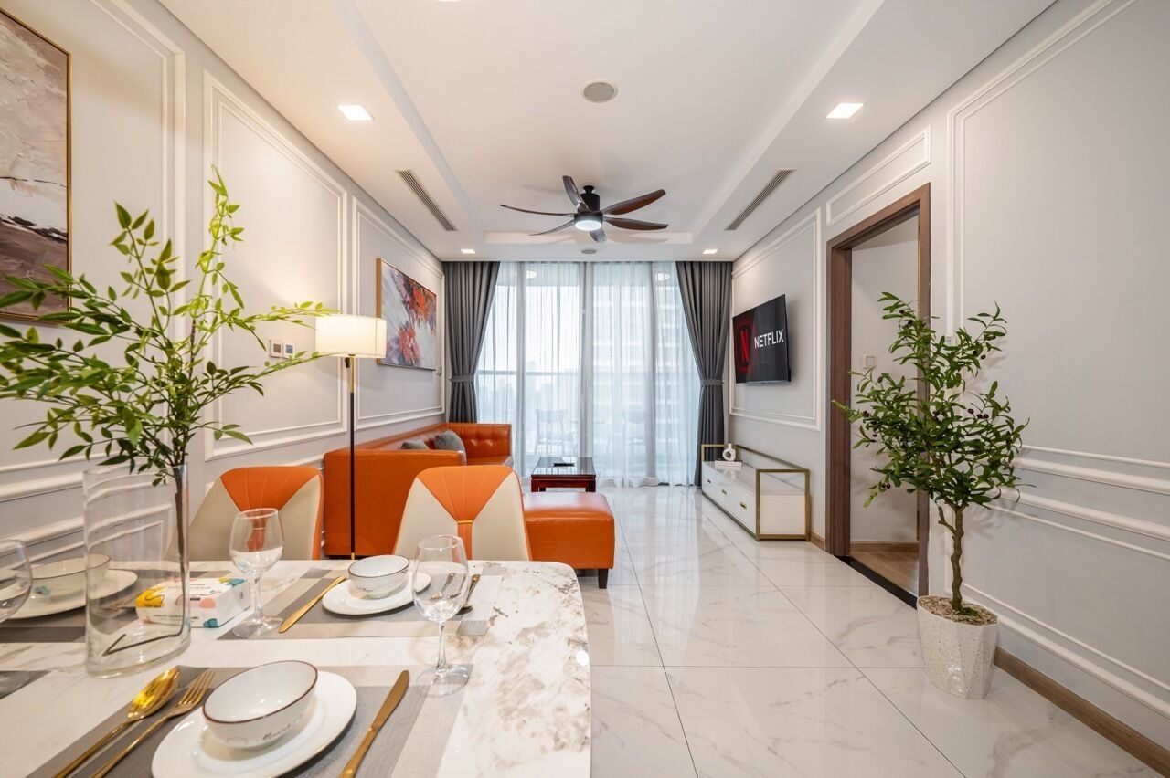 A modern hotel room with a dining area, a sofa, a television, and a ceiling fan.