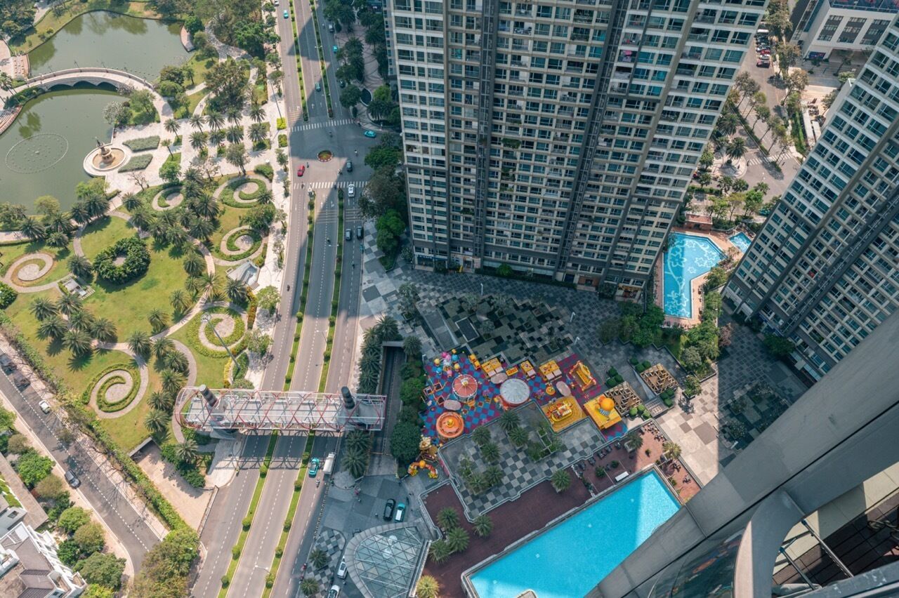 Un edificio de gran altura con piscina en la azotea y un parque ajardinado que incluye un estanque y senderos peatonales.