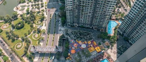 Un edificio de gran altura con piscina en la azotea y un parque ajardinado que incluye un estanque y senderos peatonales.