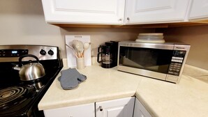 Una cocina con estufa, microondas y hervidor.