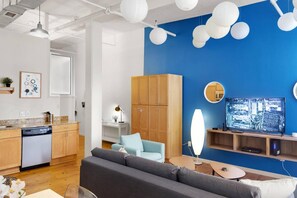 A modern living room with a blue accent wall, wooden cabinets, a grey sofa, and a television. - Loft Living in the Trendy Warehouse District (Durham)