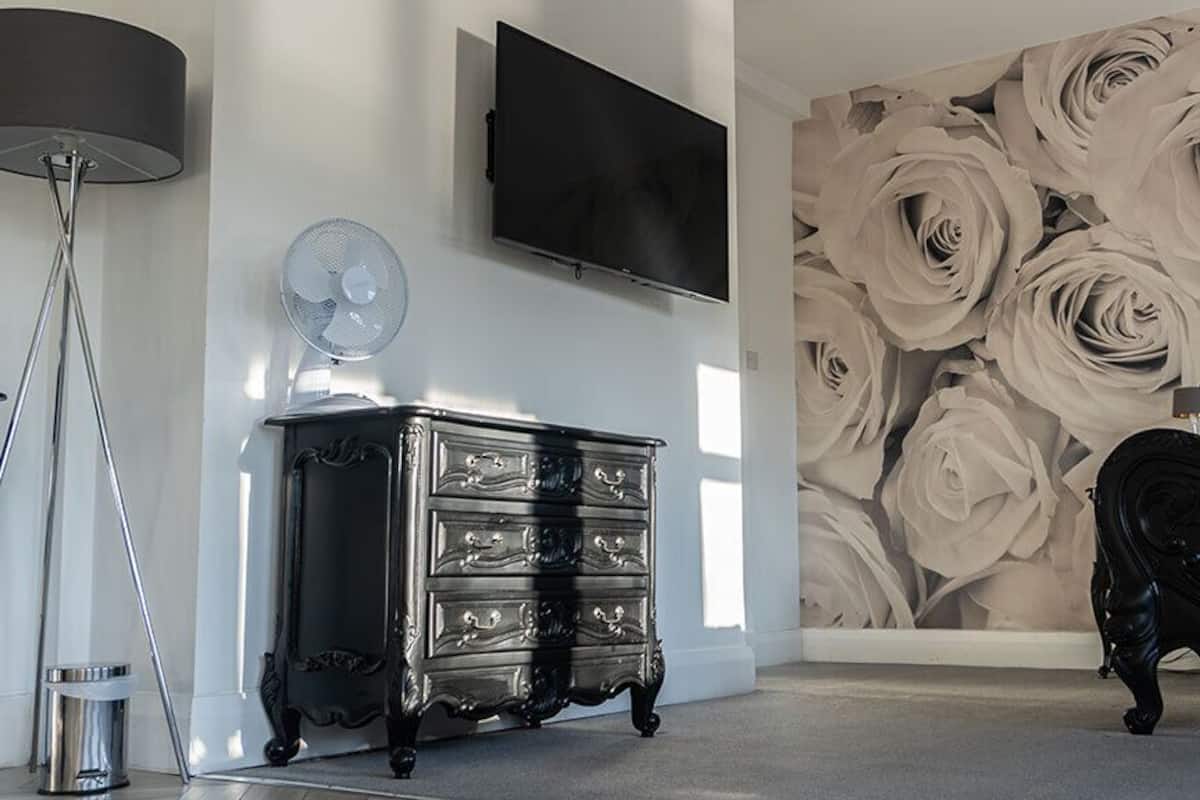 A room with a black dresser, a television mounted on the wall, and a large floral wallpaper.