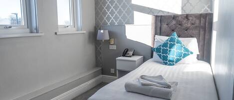 A hotel room with a bed, a bedside table with a lamp, a phone, and a window.