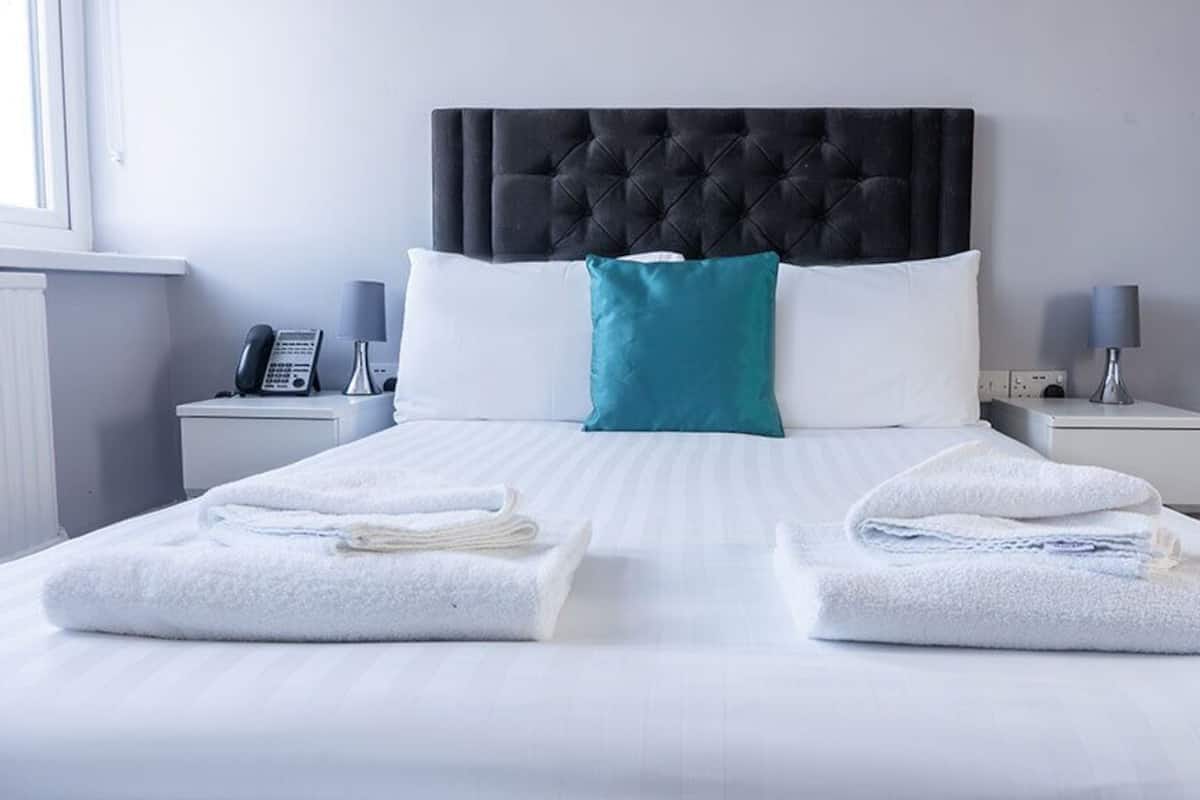 A hotel room with a bed, two bedside tables, a telephone, a lamp, and a window.