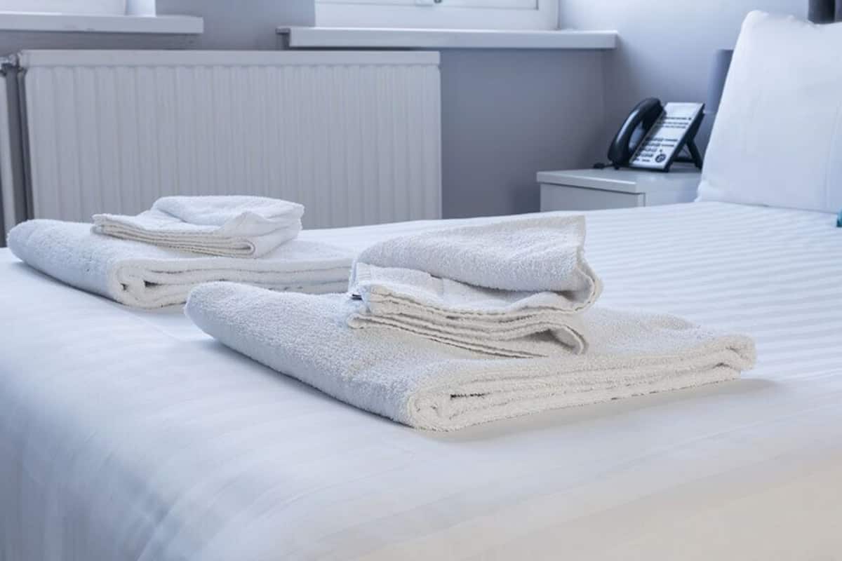 A neatly made bed with white linens and towels, a bedside phone, and a teal pillow.