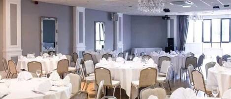 A banquet hall with round tables, chairs, and a chandelier.