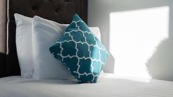 Una cama con almohadas blancas y turquesas, un cabecero capitonado y una pared lisa.