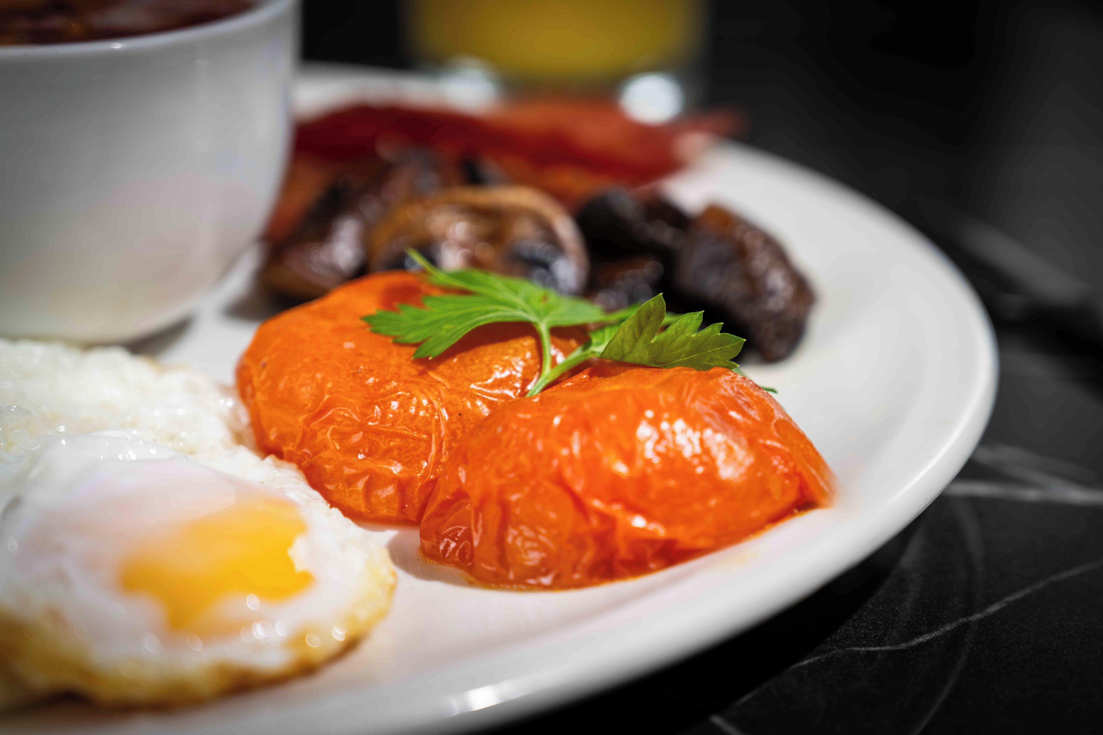 A plate with a poached egg, a stuffed tomato, and a bowl of sauce.