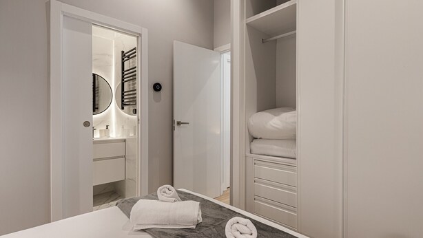 Ein modernes Hotelzimmer mit einem großen Bett, einem begehbaren Kleiderschrank und einem Badezimmer mit Spiegel und Handtuchhalter.