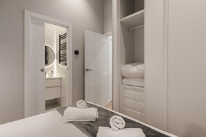 Quarto de hotel moderno com cama grande, closet espaçoso e banheiro com espelho e porta-toalhas.