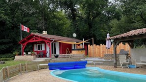 Un espace piscine avec un bâtiment rouge, une terrasse en bois et un toboggan gonflable bleu.