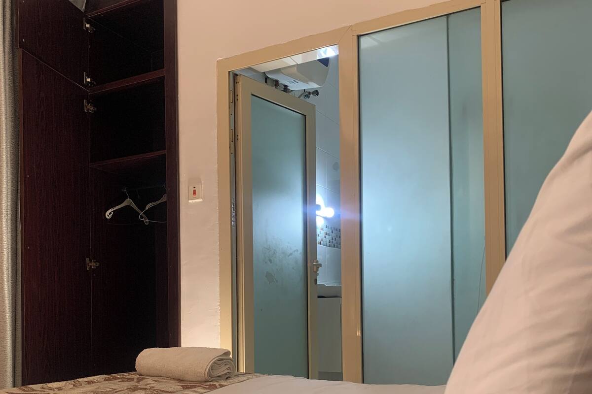A hotel room with a bed, a wardrobe, and a bathroom visible through a glass door.