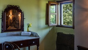 Ein Zimmer mit Schreibtisch aus Holz, einem Stuhl, einem Spiegel und einem Fenster mit Blick auf Grünflächen.