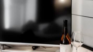 Quarto de hotel moderno com televisão de tela plana, uma garrafa de vinho e uma taça em um apoio de madeira.