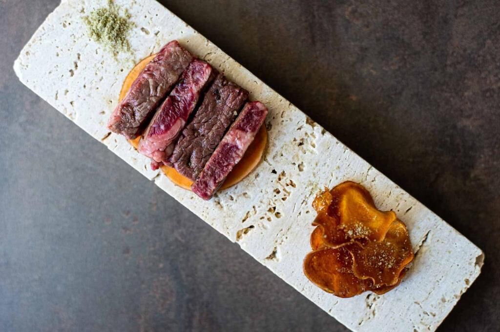 En rektangulär serveringsbricka med en bit kött och en sås.