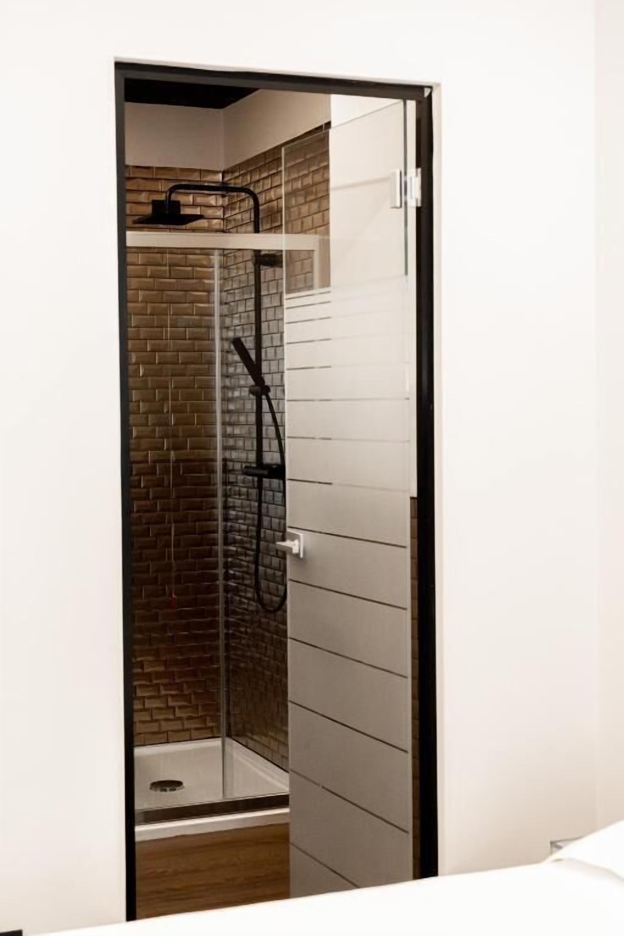 A modern bathroom with a glass shower enclosure, a visible showerhead, and a tiled wall.