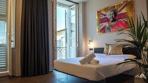 Habitación de hotel con cama, un ventanal con cortinas, un cuadro en la pared y una planta en maceta.