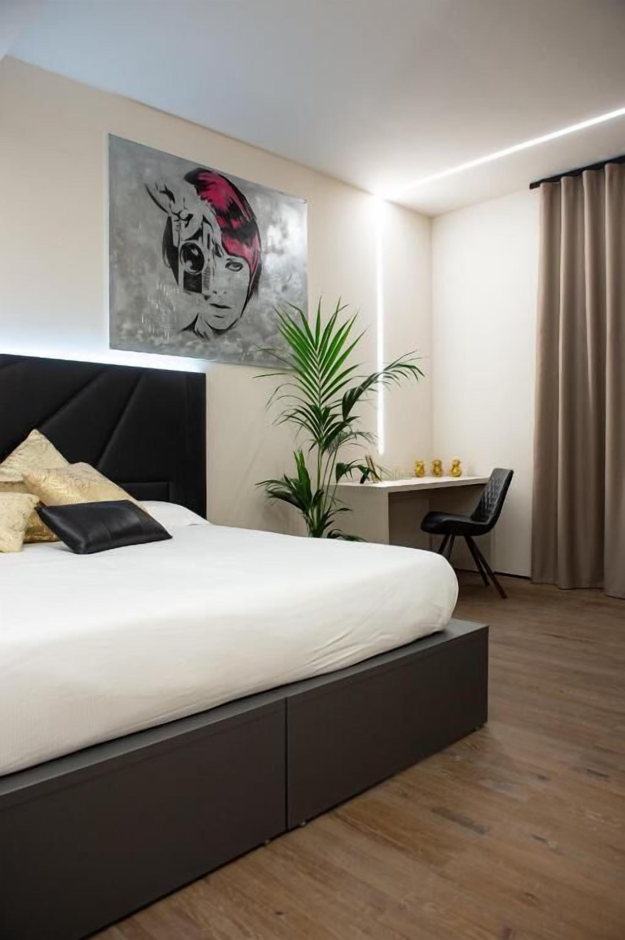 A modern bedroom with a large bed, a desk, and a potted plant.