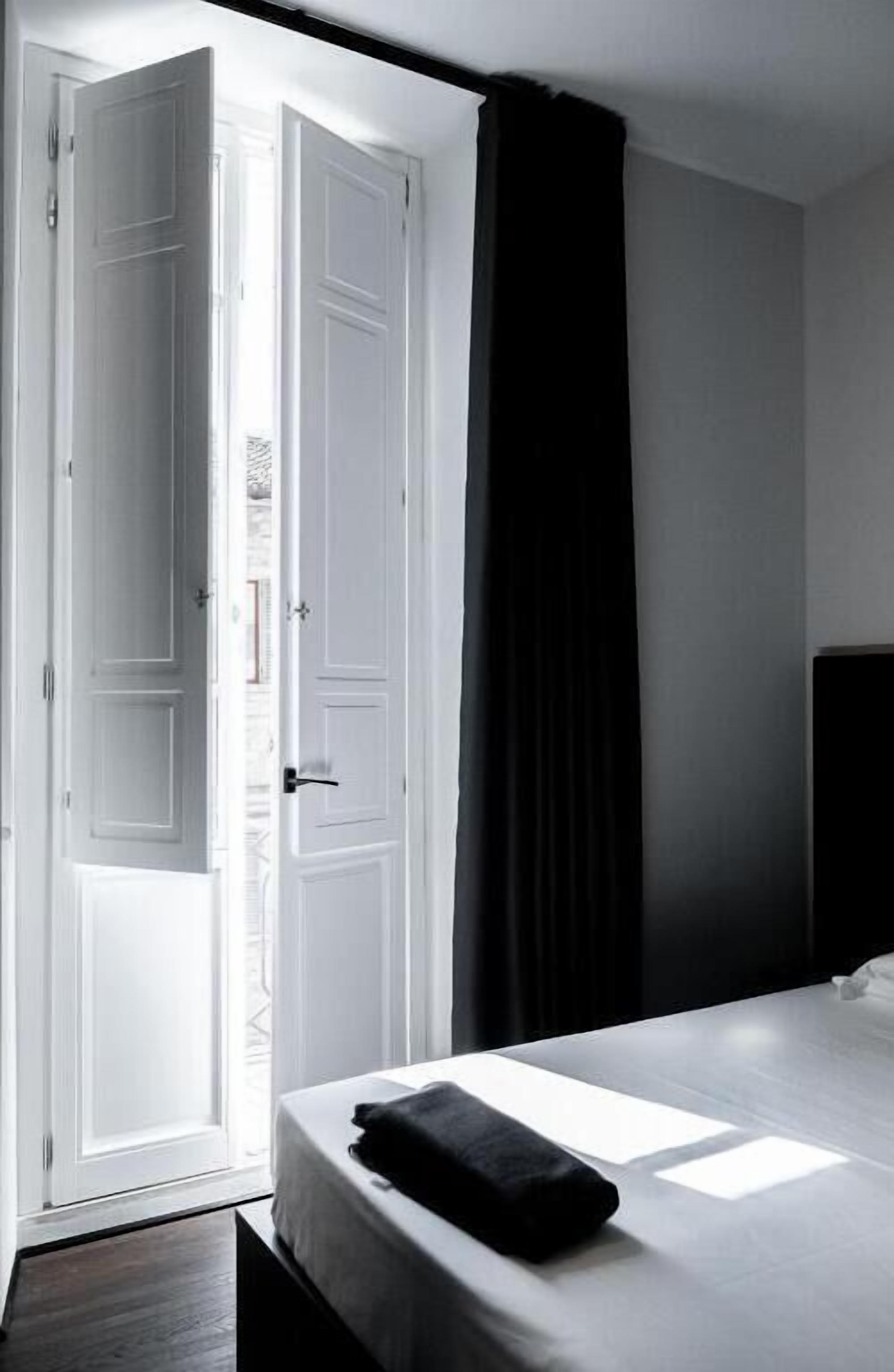 A bedroom with a bed, a white door, and a black curtain.
