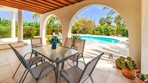 Un patio cubierto con piscina, mobiliario exterior y plantas en macetas.