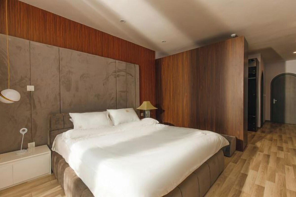 A modern bedroom with a large bed, wooden paneling on the walls, and a wooden floor.