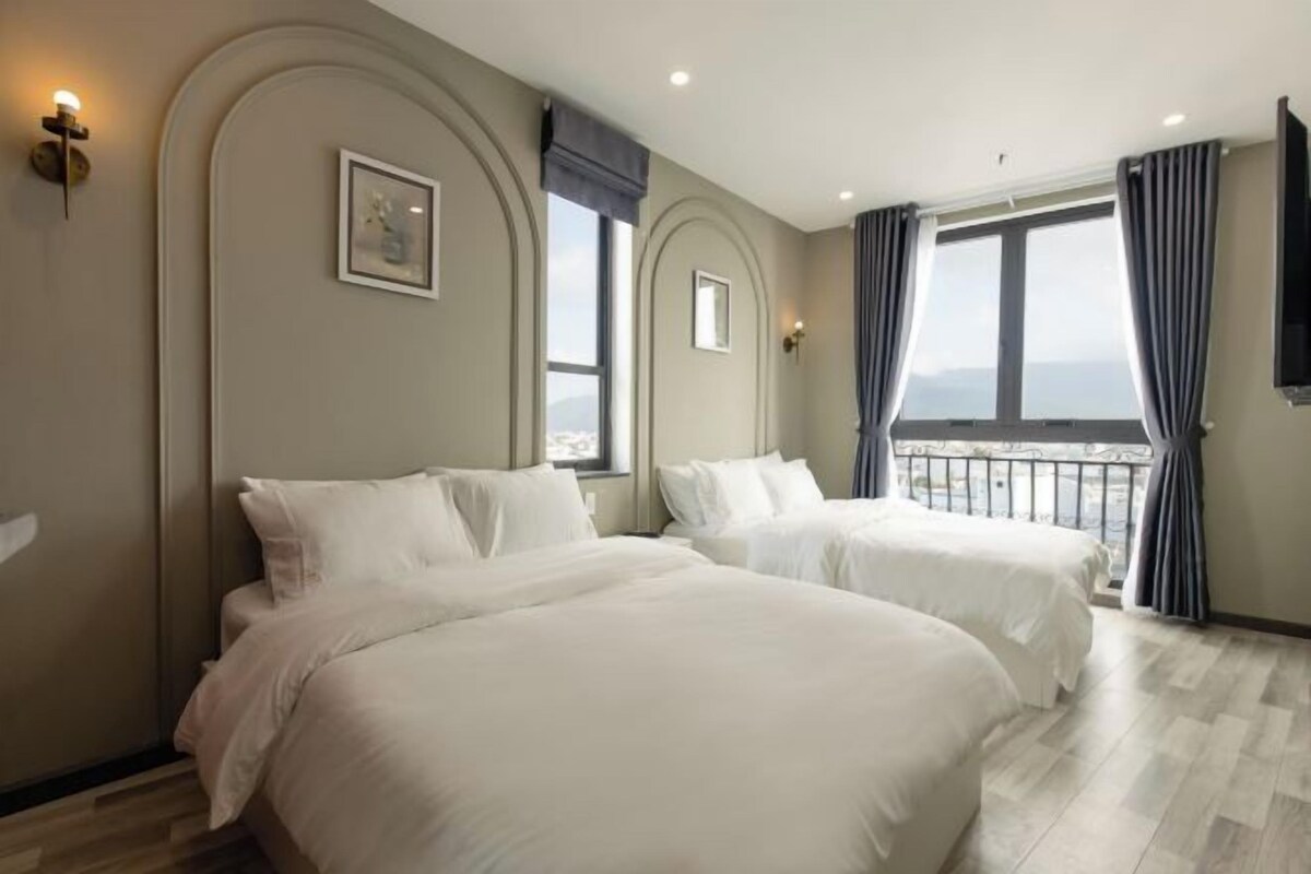 A hotel room with two beds, a balcony with curtains, and a city view.
