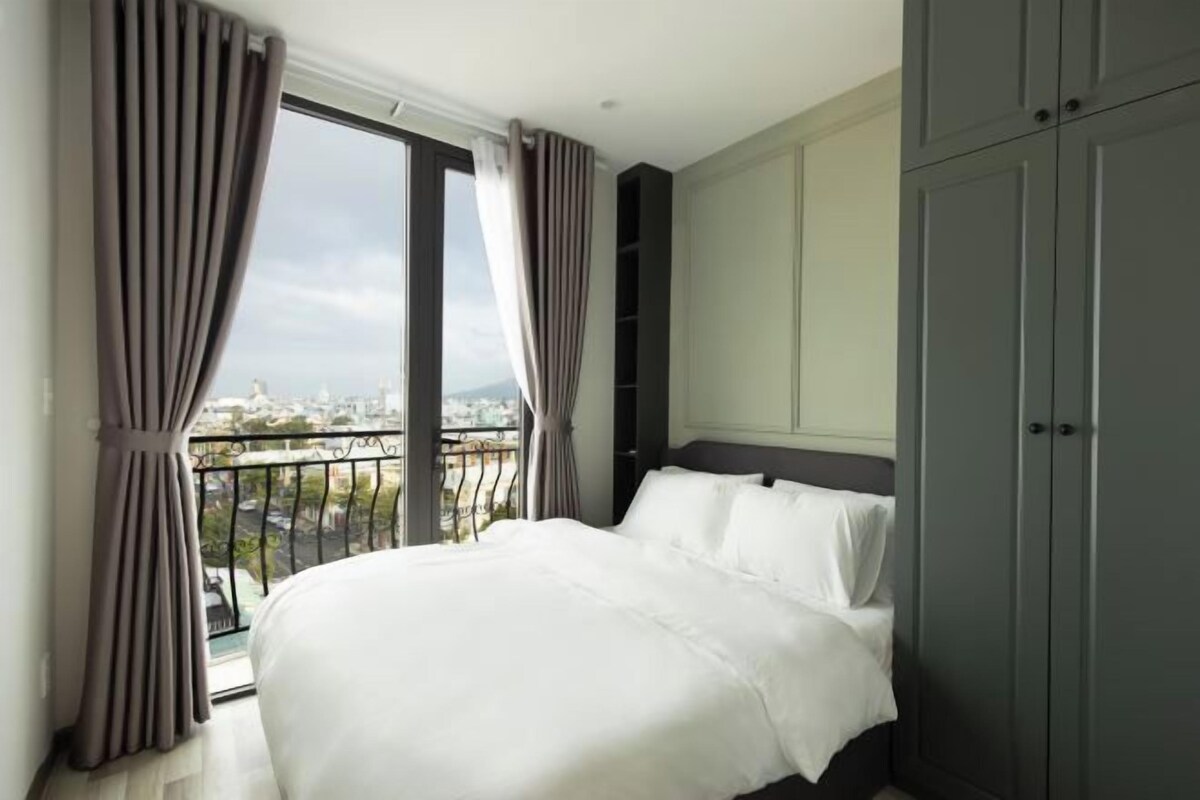 A hotel room with a large bed, grey wardrobe, and a balcony with a city view.