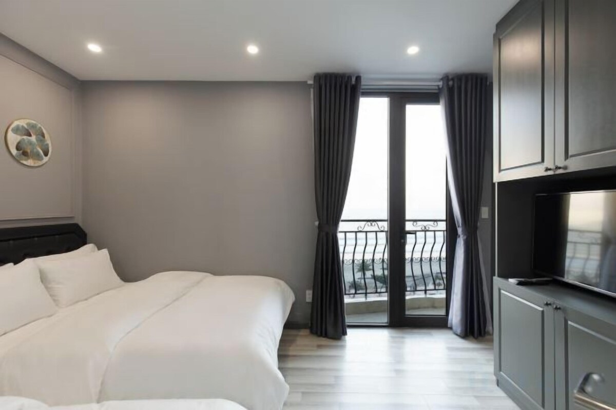 A hotel room with a bed, a television, a balcony with curtains, and a view of the outdoors.