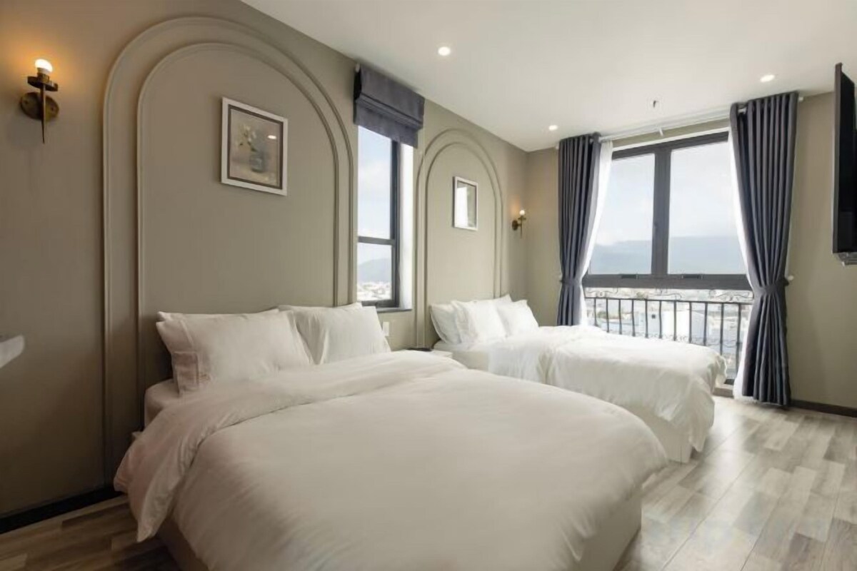 Habitación de hotel con dos camas, un ventanal con cortinas y un balcón.