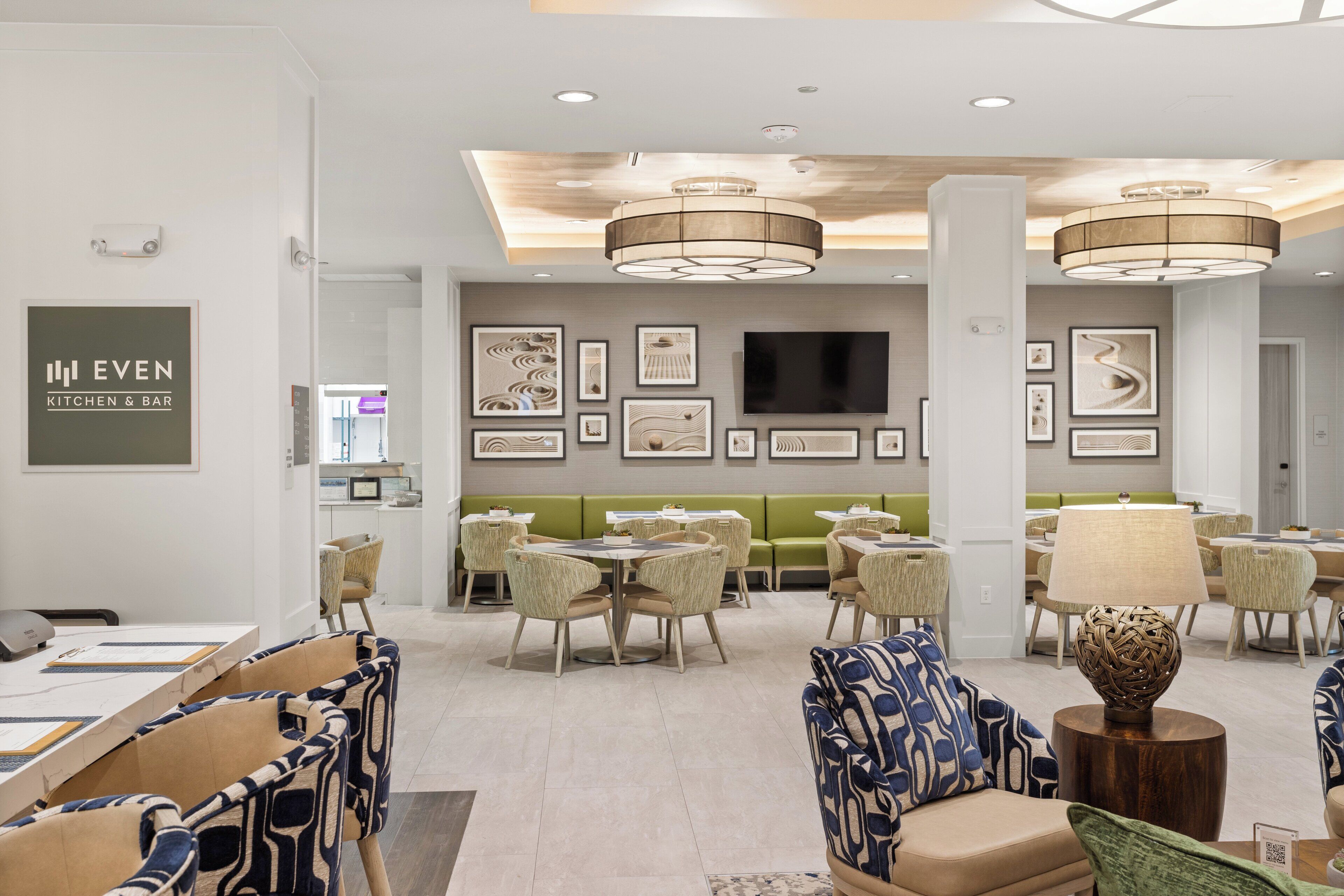 A hotel lobby with a dining area, seating arrangements, and a kitchen bar.