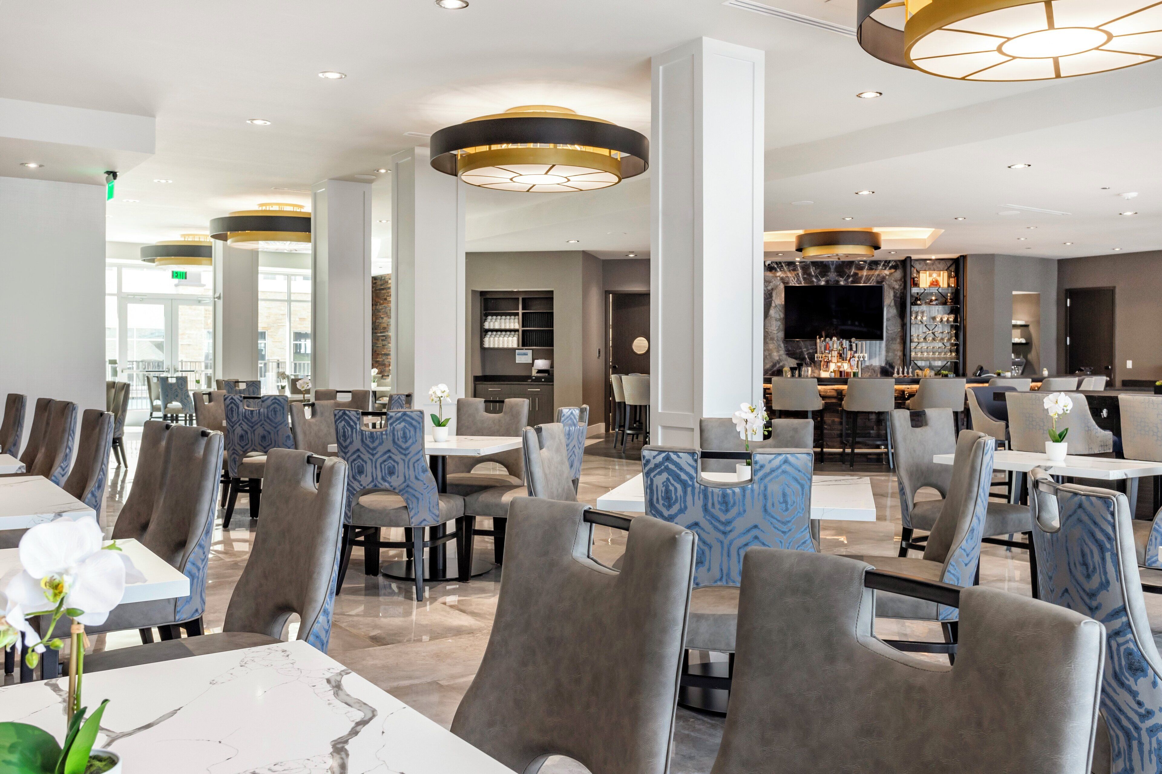 A modern restaurant with high ceilings, contemporary furniture, and a central bar area.