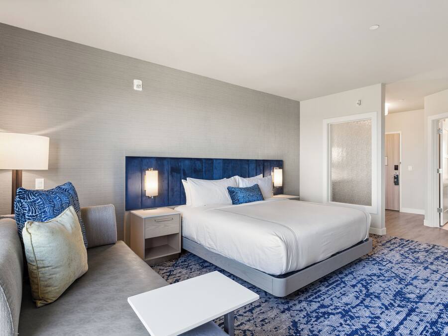 Una habitación de hotel con una cama grande, un sofá, una mesita de noche y una lámpara.