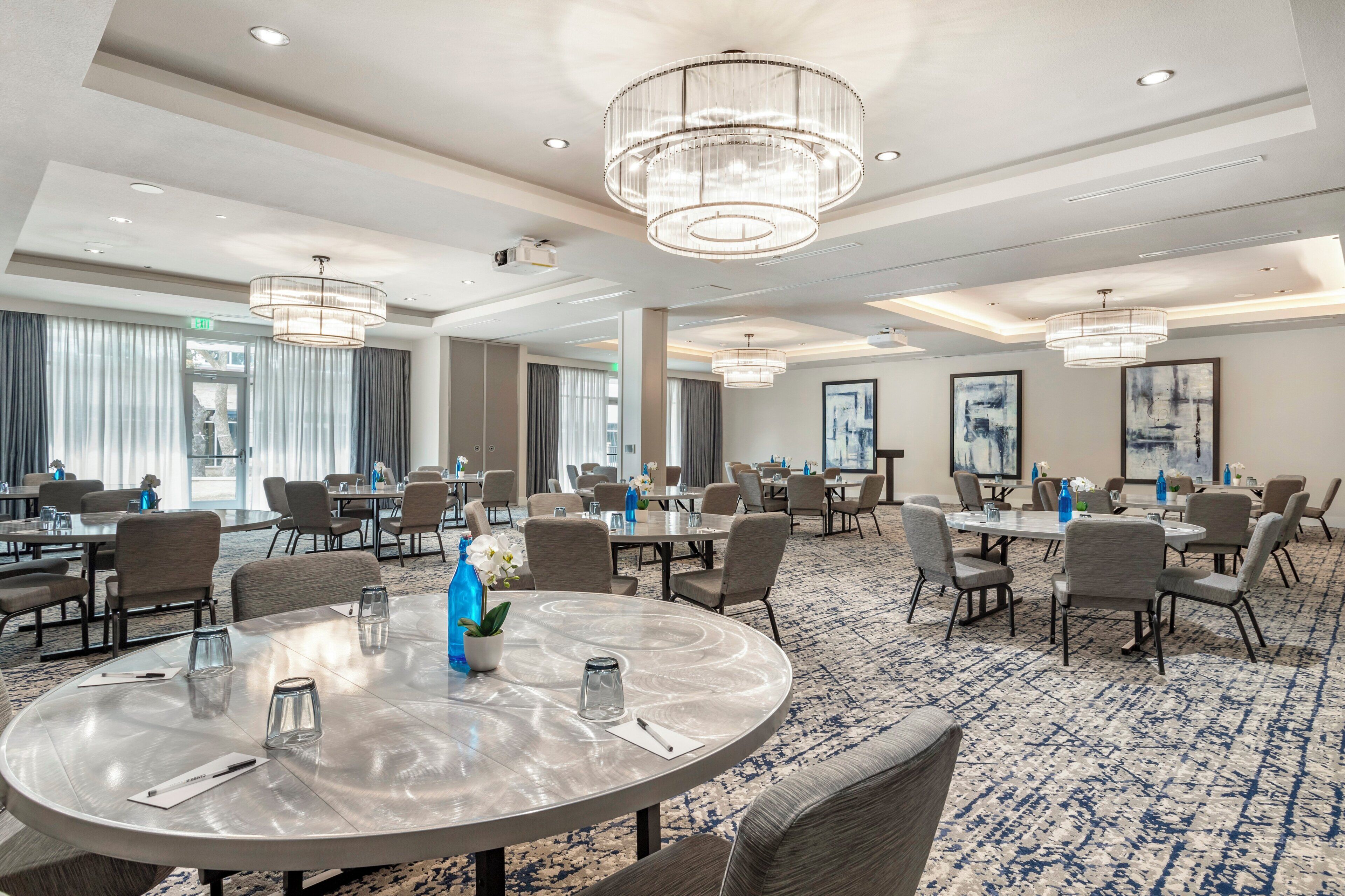 A spacious conference room with round tables, comfortable chairs, and modern chandeliers.