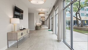 Un couloir d’hôtel moderne, avec un long comptoir d’accueil, un espace salon et de grandes fenêtres offrant une vue sur l’extérieur.