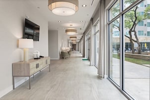 A modern hotel corridor with a long reception desk, seating area, and large windows offering views of the outdoors.