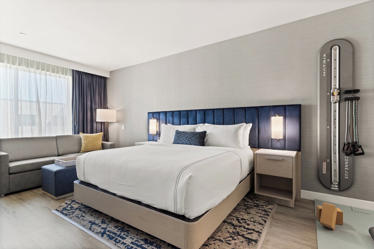 Une chambre d’hôtel moderne équipée d’un grand lit, d’un canapé, d’un bureau et d’un appareil de musculation fixé au mur.