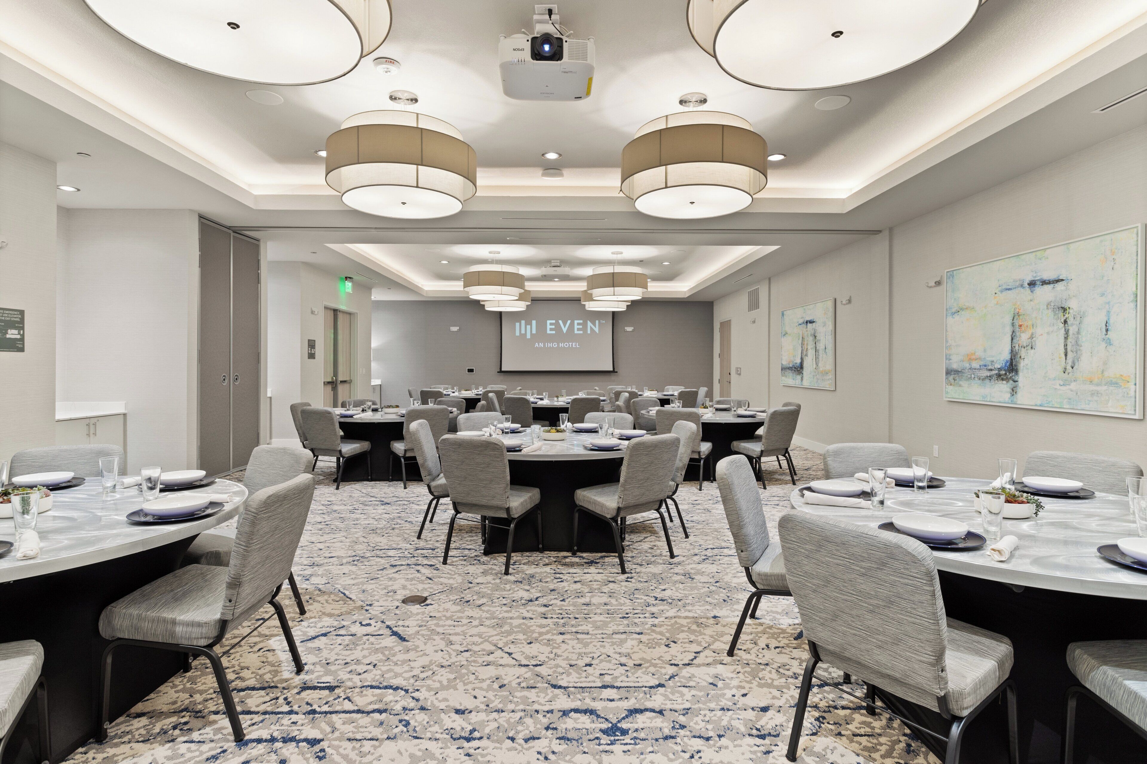 Une salle de conférence équipée de tables rondes, de chaises et d’un grand écran affichant le nom de l’hôtel.
