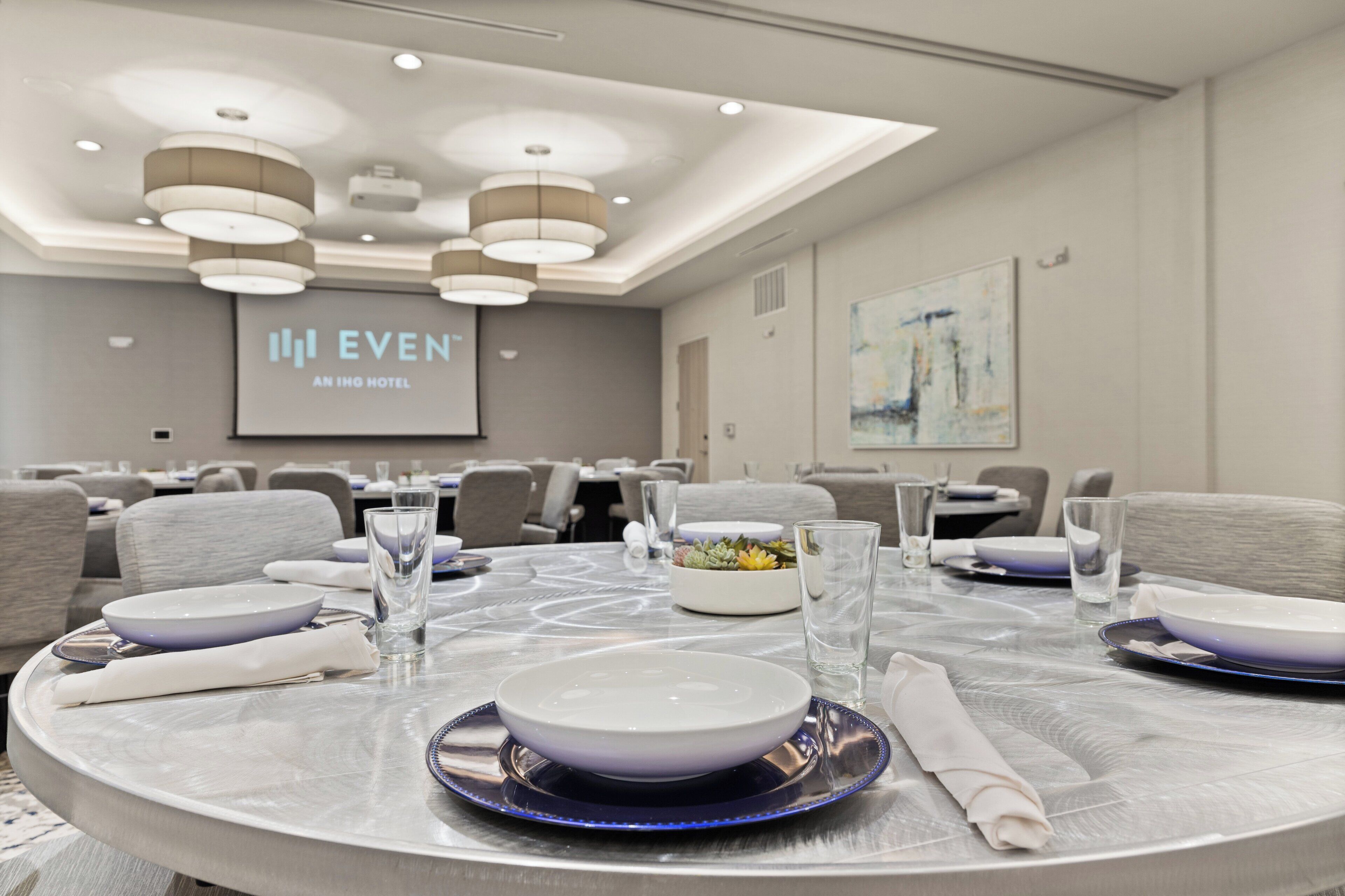 A conference room with round tables, chairs, and a projection screen displaying "EVEN AN IHG HOTEL".