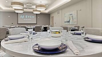 A conference room with round tables, chairs, and a projection screen displaying "EVEN AN IHG HOTEL".